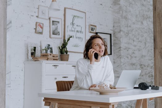 Woman in stylish home office using smartphone and laptop for communication.